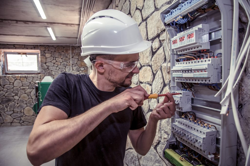 a male electrician works in a switchboard with an electrical con